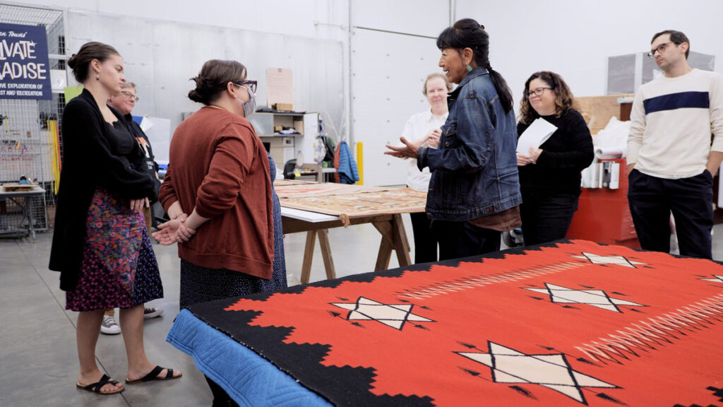 7 people in conversation over indigenous weavings